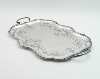 Puede incluir: Una bandeja de servir de plata con un diseño decorativo y ornamentado alrededor del borde. La bandeja tiene dos asas y una forma rectangular ligeramente redondeada.