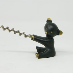 Puede incluir: Figurilla de oso de metal negro con detalles dorados que sostiene un sacacorchos plateado.