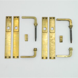 Könnte beinhalten: Ein Satz an Messing-Türbeschlägen, bestehend aus zwei Türplatten, zwei Türgriffen und zwei Rosetten. Die Beschläge sind in polierter Messing-Optik.