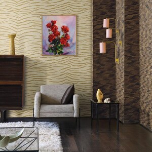May include: An interior scene featuring a framed painting of red roses, a gray armchair with a brown pillow, and a black side table. The walls have patterned wallpaper, and the floor is dark wood. Decorative lamps with pink shades are mounted on the wall.