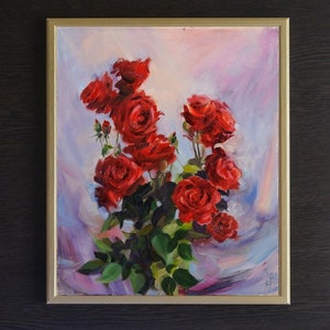 May include: Oil painting of a bouquet of red roses in a gold frame. The roses are in full bloom with green leaves and stems. The background is a soft blend of pink, purple, and white.