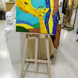 May include: A painting on a wooden easel depicts two giraffes, one adult and one baby, with a colorful abstract background. The painting is signed "L.Baga" in the bottom left corner.