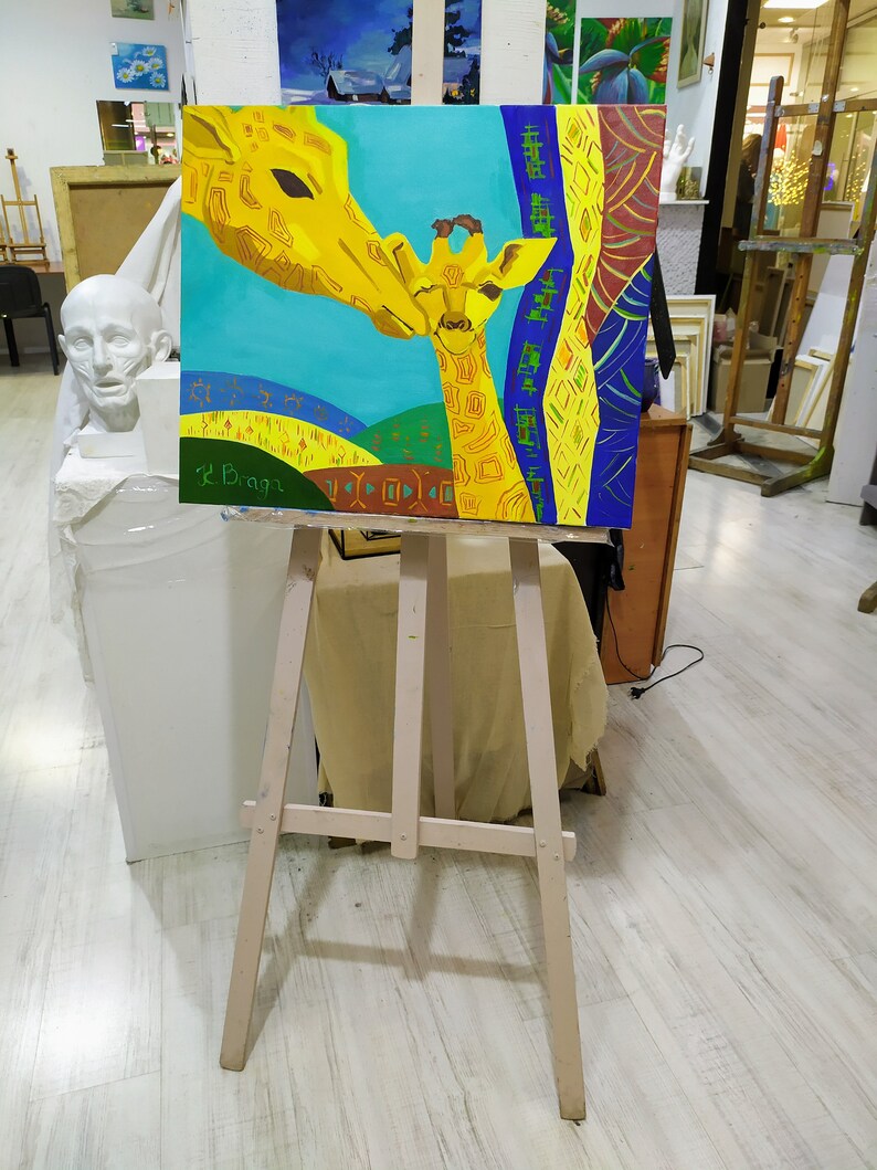 May include: A painting on a wooden easel depicts two giraffes, one adult and one baby, with a colorful abstract background. The painting is signed "L.Baga" in the bottom left corner.