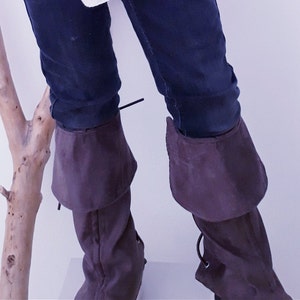 May include: A pair of brown leather boot cuffs with a fold-over design. The cuffs are worn over blue jeans.