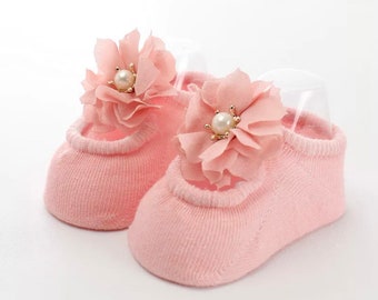 Könnte beinhalten: Ein Paar rosa Babysocken mit einer zarten Blumenverzierung an jeder Socke. Die Blumen sind aus rosa Stoff und haben eine Perle in der Mitte.