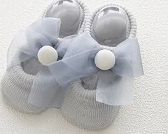 Op de afbeelding: Een paar grijze babysokken met een grote grijze tule strik en witte pompoenen op elke sok.