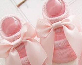 Könnte beinhalten: Ein Paar rosa Babysocken mit einer großen rosa Schleife aus Satin an jeder Socke.