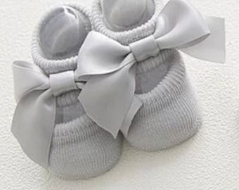 Könnte beinhalten: Ein Paar graue Babysocken mit einer großen Schleife aus Satin an jeder Socke.