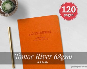 Puede incluir: Un cuaderno naranja con el texto en relieve good INKPRESSIONS LETTERPRESS Handmade Stationery. Una insignia circular roja muestra 120 pages. Un bolígrafo dorado está colocado a la izquierda. El texto Tomoe River 68gsm - CREAM - es visible.