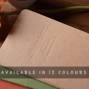 Peut inclure: Une pile de 12 cahiers de couleurs diff&eacute;rentes avec une couverture brune. Le cahier du dessus porte le texte "GOOD THINGS TAKE TIME" en relief sur la couverture. Le texte "AVAILABLE IN 12 COLOURS" est imprim&eacute; au bas de la pile.
