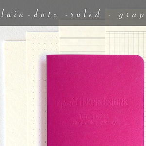 May include: A pink notebook with the text "good INKPRESSIONS" and "Journals Handmade Stationery" embossed on the cover. The notebook is sitting on top of four different types of paper: plain, dotted, ruled, and graph.