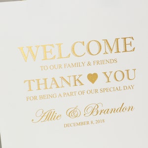 May include: White favor bag with gold ribbon handles. The bag has gold lettering that says "Welcome to our family & friends Thank You for being a part of our special day Allie & Brandon December 8, 2018".