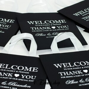 May include: Black favor bags with white satin ribbon handles. The bags have a welcome message, thank you message, and the names Alex & Brandon with the date October 6, 2018.
