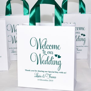 May include: White gift bag with green satin handles and the text "Welcome to our Wedding" in green cursive font. The bag also includes the names Lucia & Franco and the date 14 Dicembre 2019.