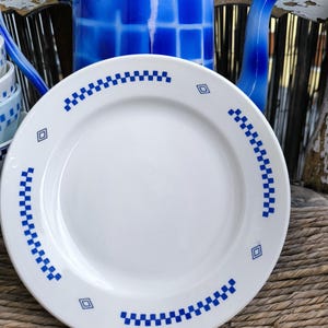 May include: A white ceramic plate with a blue and white checkered border. The plate is sitting on a woven wicker surface.