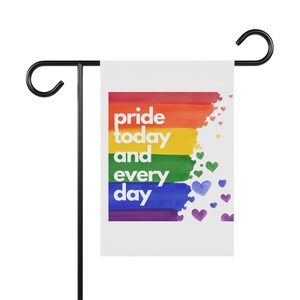 Könnte beinhalten: Eine weiße Gartenflagge mit einem Regenbogenmuster und dem Text "pride today and every day". Der Regenbogen besteht aus aquarellartigen Pinselstrichen und es sind kleine blaue Herzen um den Regenbogen verstreut.