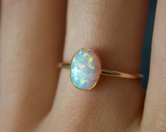 Pode incluir: Um anel de ouro com uma gema de opala oval. A opala é de cor branca leitosa com flashes iridescentes de azul, verde e rosa.