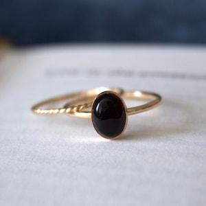 May include: A gold ring with a black oval gemstone. The ring is on a white surface.
