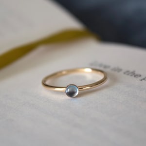 May include: A delicate gold ring with a light blue gemstone. The ring is sitting on a white page with text.