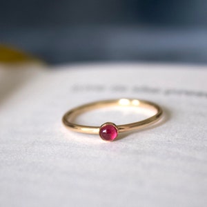 May include: A simple gold band ring with a small, round, pink gemstone.