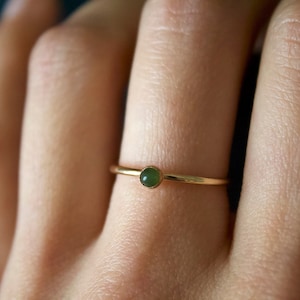 May include: A gold ring with a small, round, dark green gemstone.