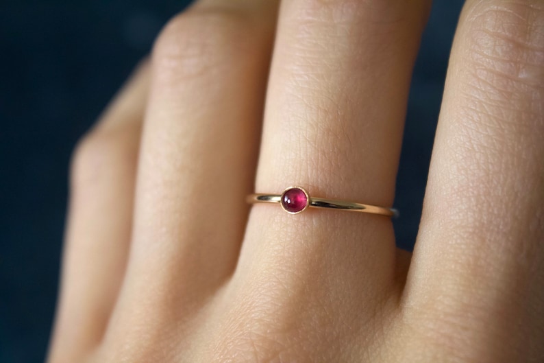 May include: A delicate gold ring with a small, round, red gemstone.