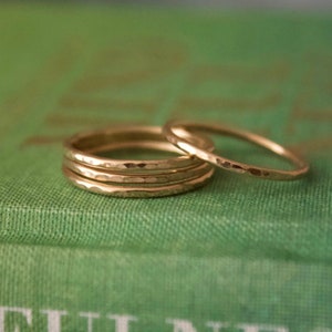May include: Four gold hammered stacking rings. The rings are stacked on top of each other and are on a green surface.