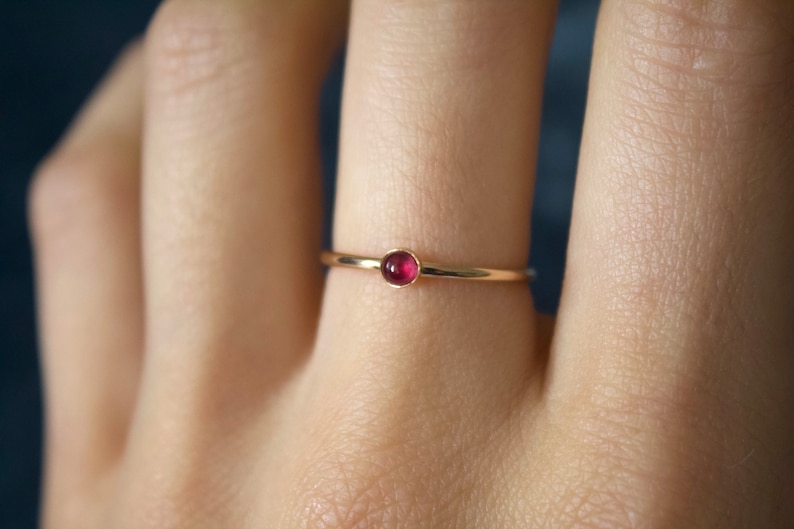 May include: A simple gold band ring with a small, round, dark red gemstone.