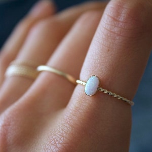 Può includere: Un delicato anello d'oro con una pietra di opale bianca. L'anello ha una fascia attorcigliata.