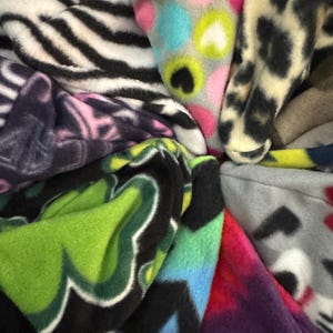 May include: A collection of colorful fleece fabrics with various patterns, including zebra stripes, hearts, and abstract designs.