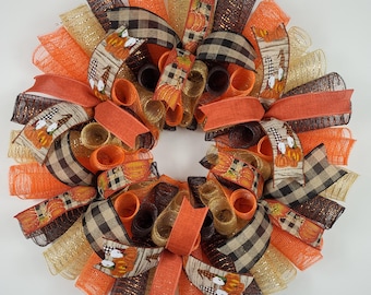 May include: A fall-themed wreath with orange, brown, and gold mesh, plaid ribbon, and a pumpkin print ribbon. The wreath is decorated with fall-themed accents.
