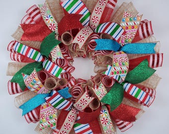 May include: A festive Christmas wreath with a circular design. It features red, green, and blue ribbons, along with ribbons with candy cane and peppermint patterns. The wreath is made with burlap and glitter accents, creating a cheerful holiday decoration.