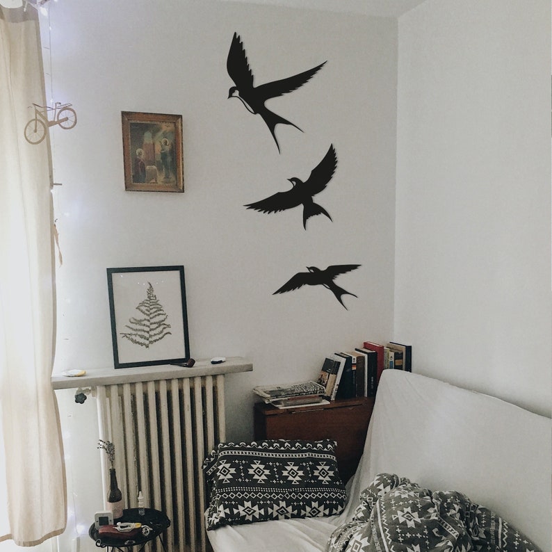 May include: Three black silhouette bird decals on a white wall. The birds are flying in a diagonal line, with the top bird at the highest point and the bottom bird at the lowest point. The birds are all facing the same direction.