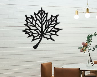 Puede incluir: Decoración de pared de metal negro en forma de hoja de arce. La hoja está detallada con líneas y venas intrincadas. La decoración está montada en una pared de ladrillo blanco.