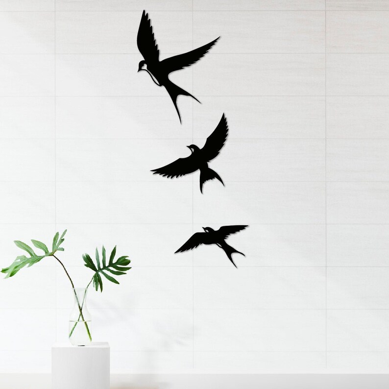 May include: Three black silhouette wall decor pieces in the shape of birds. The birds are arranged vertically, with the largest bird at the top and the smallest bird at the bottom.