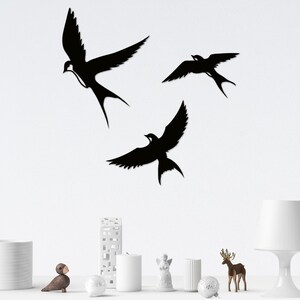May include: Three black silhouette wall decor pieces in the shape of birds. The birds are flying in different directions. The birds are on a white wall.