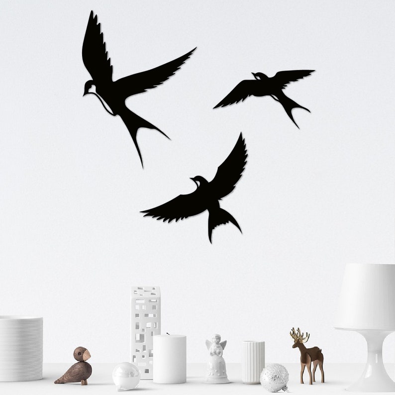 May include: Three black silhouette wall decor pieces in the shape of birds. The birds are flying in different directions. The birds are on a white wall.