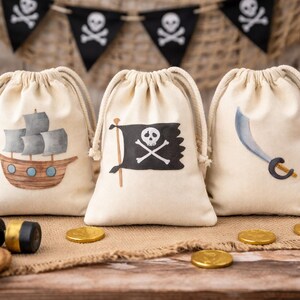 May include: Three beige drawstring bags with pirate designs. One shows a ship, another a skull and crossbones flag, and the third a cutlass. Gold coins and a pirate flag are arranged around the bags.