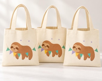 May include: Three off-white canvas tote bags, each featuring a brown sloth illustration hanging from a colourful triangular bunting banner with small purple stars printed above the sloth on the front of the bag.