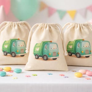 Op de afbeelding: Drie beige trekkoordzakken met een schattig groen vuilniswagenontwerp. De zakken staan op een wit oppervlak met kleurrijke snoepjes en feestversieringen op de achtergrond. De vrachtwagen heeft een hartje op de zijkant.