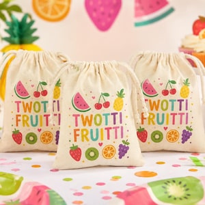 May include: Three off-white drawstring favor bags made of fabric, each featuring the colorful text TWOTTI FRUITTI and illustrations of various fruits including watermelon, cherries, pineapple, strawberry, kiwi, orange, and grapes.
