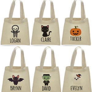 May include: Six beige canvas tote bags with white handles. Each bag features a different Halloween-themed graphic: a skeleton, black cat, jack-o'-lantern, bat, Frankenstein's monster, and ghost. Each design is paired with a name: Logan, Claire, Tucker, Brynn, David, and Evelyn.