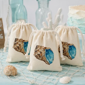 Könnte beinhalten: Drei beige Geschenktüten mit Kordelzug und Muscheldesign. Die Taschen haben ein Aquarellbild einer braunen und blauen Muschel. Ein Holzschild sagt "THANK YOU for CELEBRATING with us!"