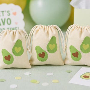 May include: Three small, off-white drawstring bags with green avocado illustrations, each featuring a yellow heart and a brown heart. The bags are arranged on a light green surface, with confetti and a sign that says "Thank You!"