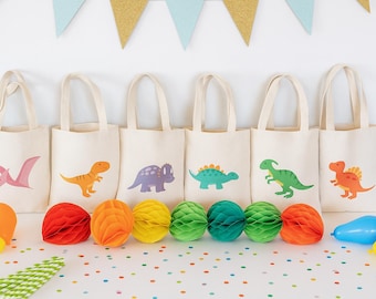 Puede incluir: Seis bolsas de tela de color blanco roto, cada una con una ilustración de dinosaurio de diferente color. Las bolsas están dispuestas en fila, acompañadas de bolas de papel de nido de abeja rojas, naranjas, amarillas, verdes y azules.