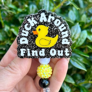 May include: Black and yellow glitter badge holder with a yellow rubber duck and the text "Duck Around Find Out".