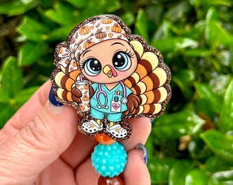 May include: A badge reel featuring a cartoon turkey dressed as a healthcare worker in teal scrubs with a stethoscope, holding a pumpkin-patterned tumbler. The turkey wears a matching pumpkin print cap and white clogs, accented by brown glitter.