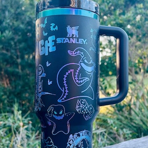 May include: Black stainless steel travel mug with a black handle and a black and iridescent lid. The mug has a graphic print of characters from the movie "The Nightmare Before Christmas". The text "What have we got here?" is printed on the mug. The mug is sitting on a wooden surface.