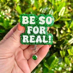 May include: Green glitter badge holder with the text "BE SO FOR REAL!" in white letters.