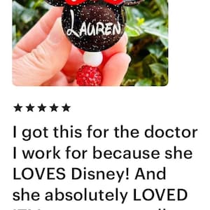 May include: A black and red Minnie Mouse-themed name tag with glitter and white polka dots. The name "Lauren" is written in white on the tag.